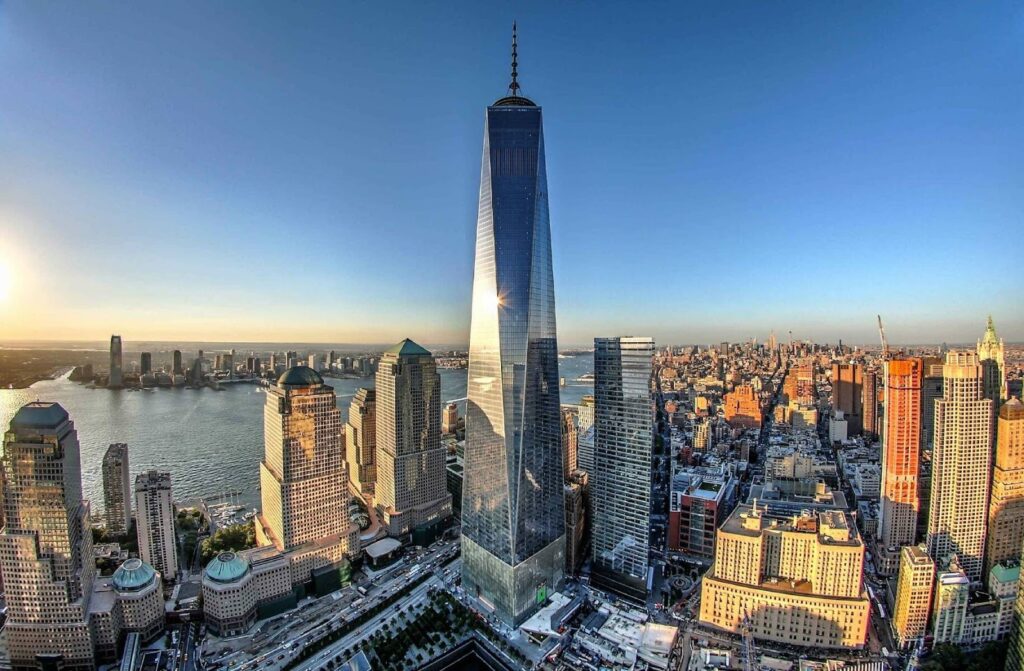 One World Trade Center skyscraper in Lower Manhattan, New York City, rising above the surrounding skyline near the Hudson River on a clear day.