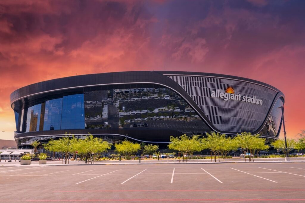 Allegiant Stadium exterior view in Las Vegas, Nevada, showing the modern black glass façade and curved stadium architecture under a colorful sunset sky.